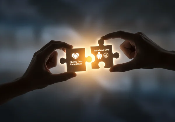 Two hands connecting puzzle pieces with love language icons.